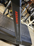 Three-quarter angle studio shot of an AssaultRunner Elite curved treadmill showing the built-in storage compartments and multi-position handrails.